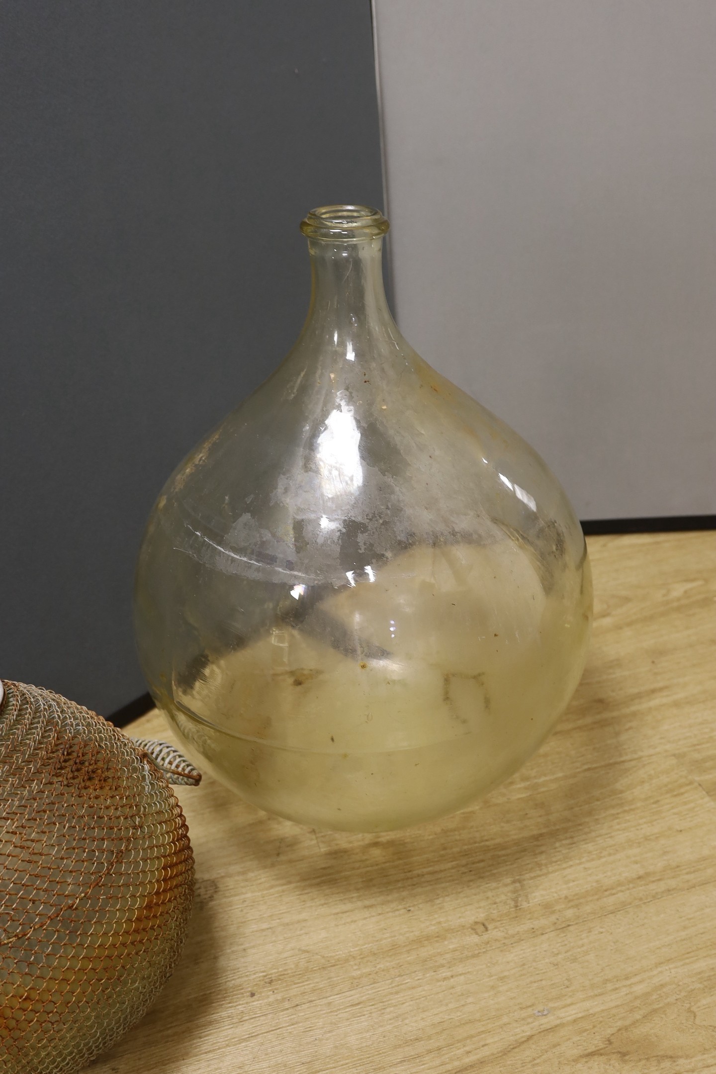 A large clear glass carboy and unusual wire-mounted glass carboy, largest 28cms high.